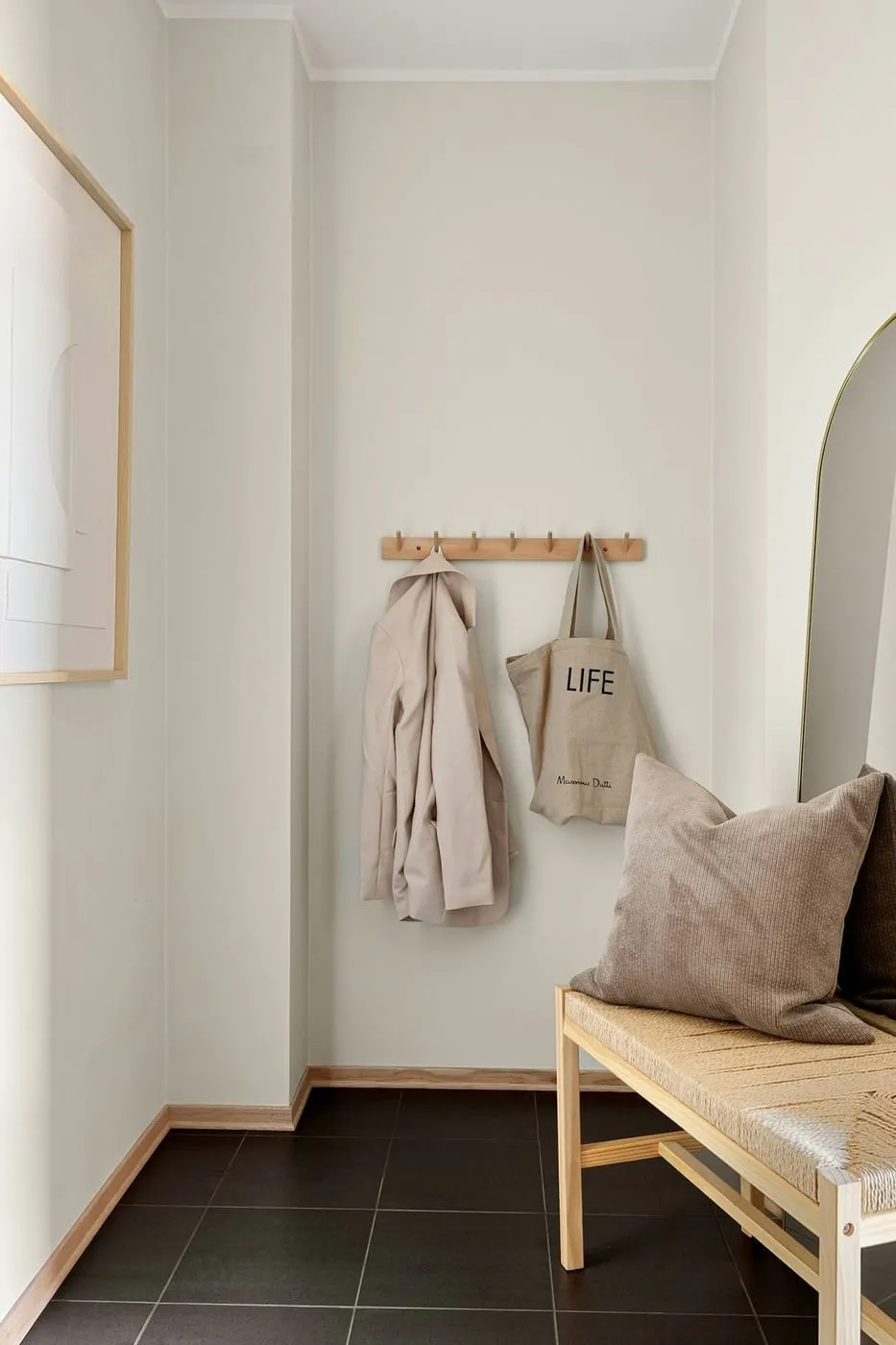 A renter-friendly hallway with coats and a bag hung on a wall-mounted peg rail beside a leaned arched mirror